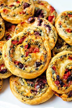 many small pastries on a white plate with red peppers and black olives in the middle