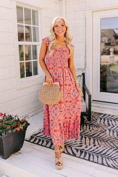 a woman standing on the porch with her hand in her pocket and wearing a pink floral dress