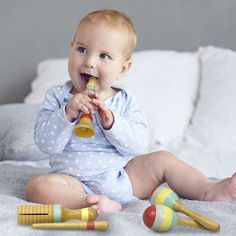 a baby is sitting on the bed playing with toy rattlers and toothbrushes