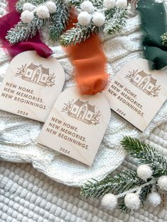 three new home tags on a white blanket with pine branches and snowflakes around them