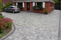 a car is parked in front of a brick house with flowers on the driveway and landscaping around it