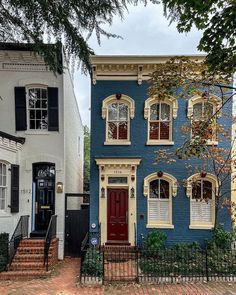 a blue house with red door and windows on the street in front of other houses