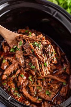 a wooden spoon full of shredded beef and garnished with parsley in a slow cooker