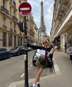 a woman standing next to a street sign in front of the eiffel tower