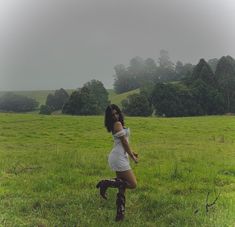 a woman in a white dress and boots is standing on the grass with her legs crossed