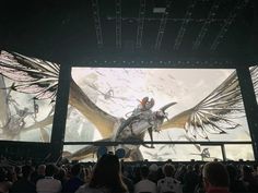 a large screen with an image of a giant bird on it's side in front of a crowd