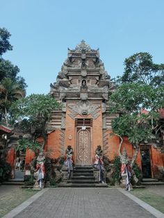 the entrance to an old building with statues on it's sides and trees in front