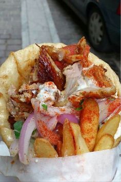 a close up of a sandwich with meat and french fries on a paper wrapper