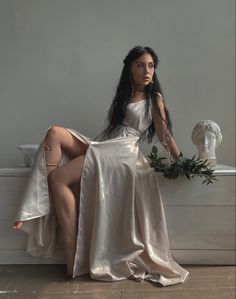 a woman in a white dress sitting on top of a table next to a vase