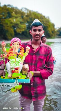 a man standing in the water holding a cake decorated with ganeshi and other figurines