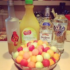 a glass bowl filled with fruit next to bottles of alcohol and other items on a counter