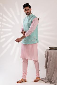 Aqua blue sleeveless bundi with bloom embroidery using beads and pearls. Paired with long sleeves pink kurta and churidar.
Components: 3
Pattern: Embroidered
Type Of Work: Bloom
Neckline: Mandarin Collar
Sleeve Type: Bundi: Sleeveless, Kurta: Long
Fabric: Mal Cotton, Raw Silk, Cotton Lycra
Color: Blue, Pink
Other Details: 
Approx weight: 2kgs
Poly lining
Occasion: Mehendi and Puja, Sangeet - Aza Fashions Designer Sleeveless Kurta With Dori Work, Sleeveless Nehru Jacket With Zari Work For Wedding, Designer Sleeveless Kurta For Spring, Spring Designer Chanderi Nehru Jacket, Designer Sleeveless Bandhgala With Resham Embroidery, Designer Sleeveless Bandhgala With Zari Work, Sleeveless Bandhgala With Resham Embroidery For Festive Occasions, Sleeveless Embroidered Bandhgala For Eid, Embroidered Sleeveless Bandhgala For Eid