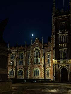 an old building lit up at night with the moon in the sky