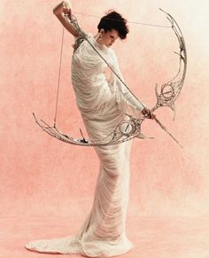 a woman dressed in white holding a bow and arrow