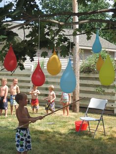 a group of kids playing in the yard with some balloons hanging from a line above them