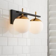 two light fixtures mounted on the wall in a white tiled bathroom with black and gold accents