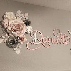 the name danielle is made out of pink and grey paper flowers on a gray wall