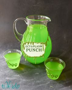 a green pitcher and two cups sitting next to each other on a gray surface with the words ectsplasm punch painted on it