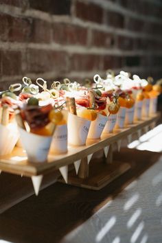 small cups filled with food sitting on top of a wooden tray next to a brick wall