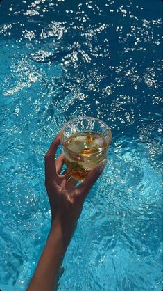 a hand holding a wine glass in front of a swimming pool filled with blue water