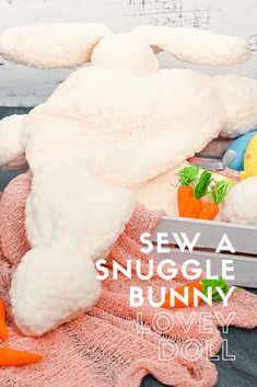 a stuffed bunny sitting on top of a blanket next to carrots and an orange