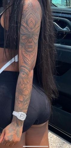 a woman with long hair and tattoos on her arm standing in front of a car