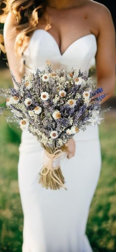 a woman in a white dress holding a bouquet of wildflowers and lavender flowers