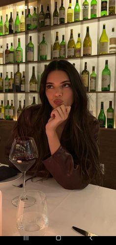 a woman sitting at a table with a wine glass in front of her and bottles behind her