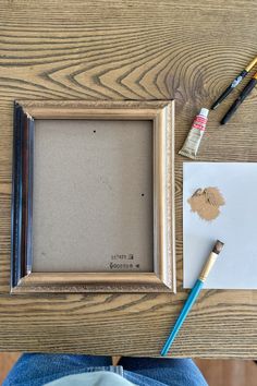 a person sitting at a table with some paint and pencils next to an empty picture frame