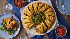 a table topped with plates and bowls filled with food next to pizzas on top of blue napkins