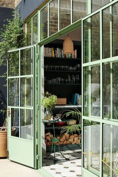 an open green door leading into a room with lots of plants and bookshelves