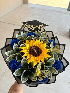 a hand holding a bouquet of dollar bills and a sunflower with congratulations written on it