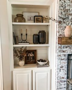 a white book shelf filled with vases and other items next to a brick wall