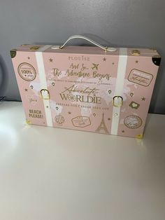 a pink and white suitcase sitting on top of a table next to a clock with the words worldie written on it