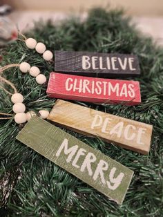 three wooden signs on top of a christmas tree with ornaments around them and the words believe, christmas, peace, merry