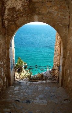 an open door leading to the ocean from a stone building with wrought iron railings