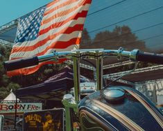 an american flag is flying in the background as a vintage motorcycle sits parked near a fairground