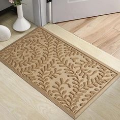 a beige door mat sitting on the floor next to a white vase with flowers in it