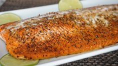 a close up of a piece of fish on a plate with lemons and lime slices