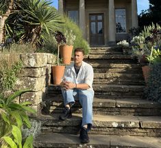 a man sitting on steps in front of a house with potted plants next to him