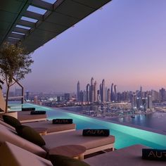 an outdoor pool overlooking the city skyline at dusk, with lounge chairs and pillows on it