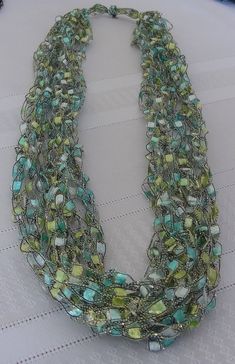 a multi strand necklace with green and blue glass beads on a white tableclothed surface