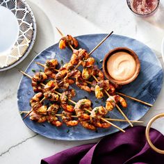 several skewers of food on a blue plate with dipping sauce in the middle