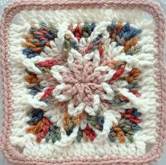 a crocheted square with a flower on the center is shown in pink and white