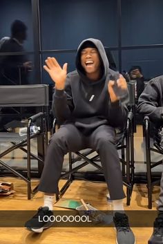 two people sitting in chairs with their hands up and one person wearing a hoodie