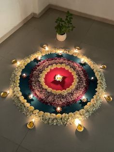 a flower arrangement on the floor with candles and lights around it in front of a potted plant