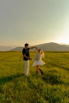 a man and woman standing in the middle of a field holding each other's hands