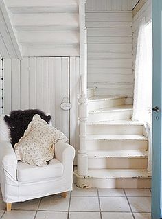 a white chair sitting in front of a wooden stair case next to a door and window