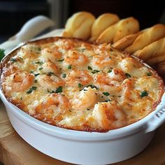 a white casserole dish with shrimp and bread sticks in the background on a cutting board