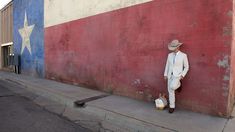 a man in a white suit and hat leaning against a wall with the american flag painted on it